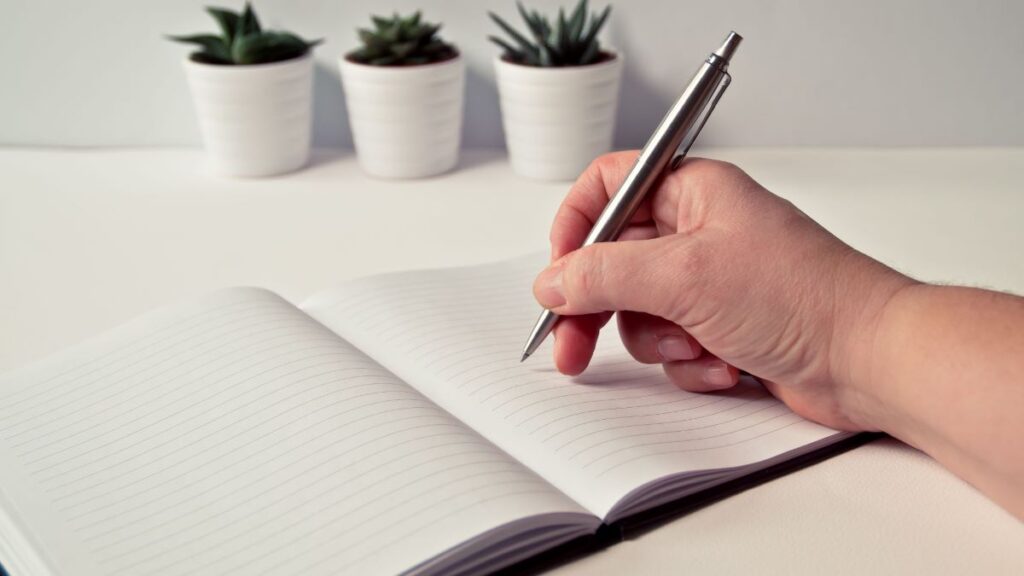 hand holding a pen over a journal